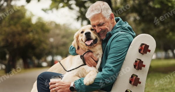 A man kneeling in a park, arms wrapped around a dog, forehead resting against its neck